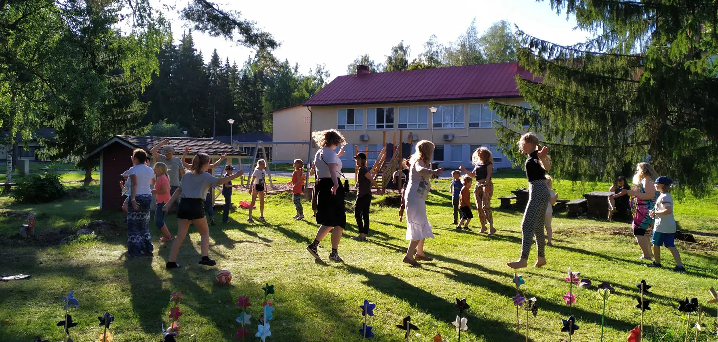 Leirin iltaohjelmassa lapset ja isoset tanssivat ja hyppivät nurmikolla opiston takapihalla.